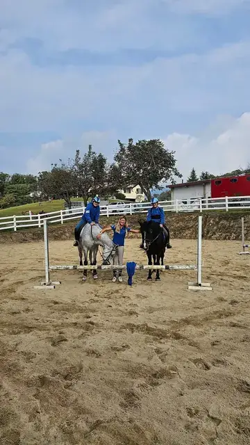 Due giovani allievi a cavallo con l'istruttrice nel campo esterno con ostacoli del maneggio