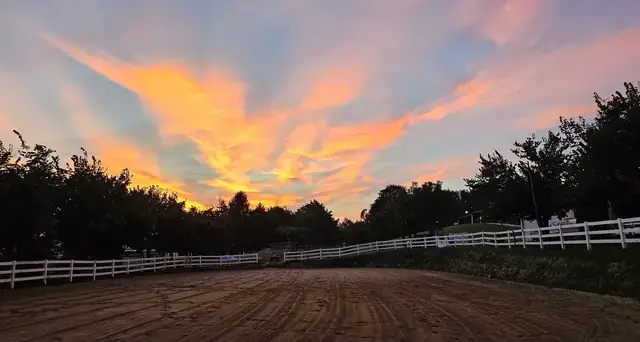 Campo di equitazione con staccionata bianca sotto un cielo infuocato al tramonto a Mitena Ranch