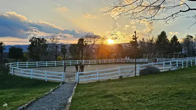 Tramonto sul campo esterno con staccionata bianca, istruttori e un cavallo al centro della pista