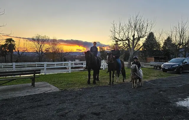 Due cavalieri e un bambino su un pony al guinzaglio davanti al tramonto sul maneggio
